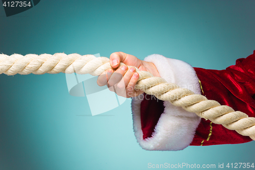 Image of Hand of Santa Claus pulling the rope on blue background