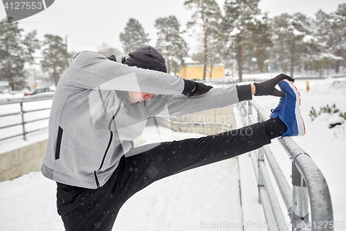 Image of sports man stretching leg at fence in winter