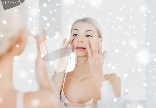 Image of happy woman applying cream to face at bathroom