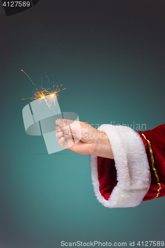 Image of Hand of Santa Claus holding a sparklers on blue background