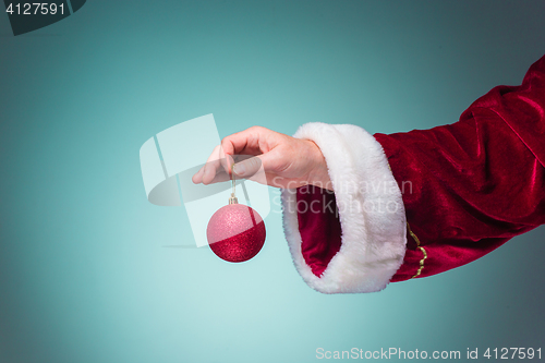 Image of Hand of Santa Claus holding a Christmas ball on blue background