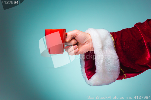 Image of Hand of Santa Claus holding a red cup on blue background