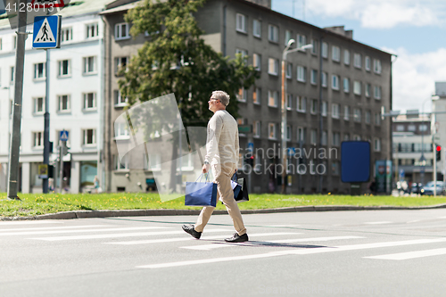 Image of senior man with shopping bags walking on crosswalk