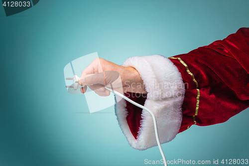 Image of Hand of Santa Claus holding a electrical plug on blue background