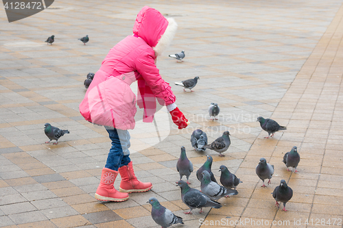 Image of girl in a pink jacket is feeding bread to the pigeons Square