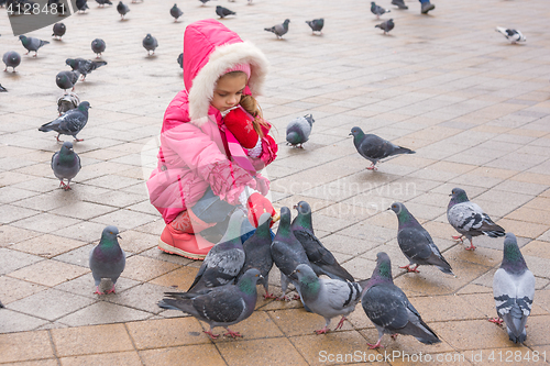 Image of Seven-year girl in the winter feeding pigeons in the street