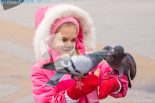 Image of girl in a pink jacket watching the pigeons that sit on her hands
