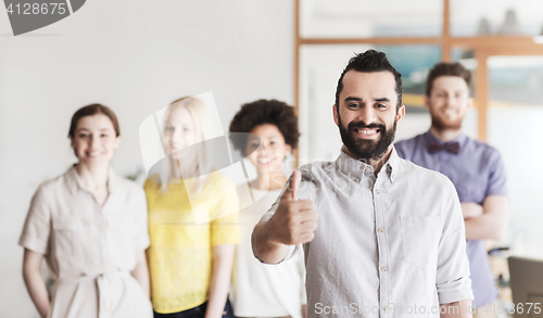 Image of happy man showing thumbs up over team in office