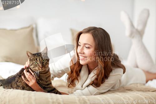 Image of happy young woman with cat lying in bed at home