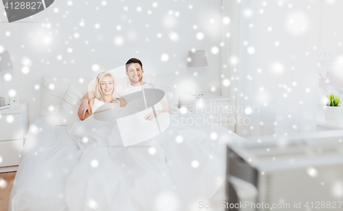 Image of happy couple lying in bed at home and watching tv