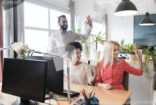 Image of happy creative team waving hands in office