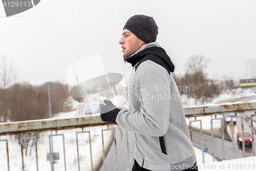 Image of man in earphones running along winter bridge