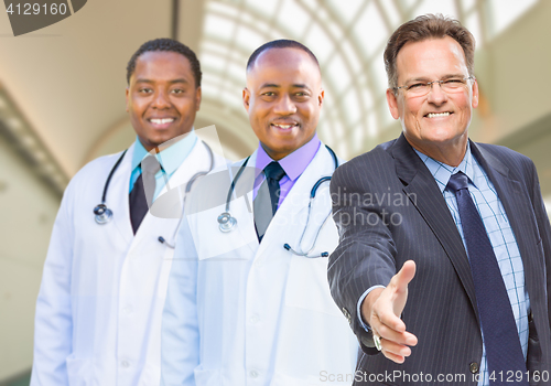 Image of Mixed Race Doctors Behind Businessman Reaching for Hand Shake In