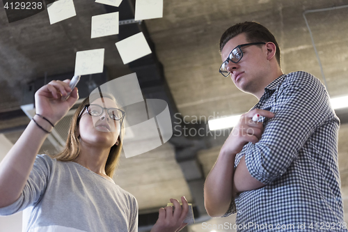 Image of young couple at modern office interior writing notes on stickers