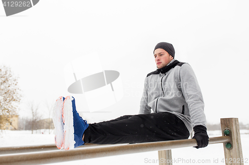 Image of young man exercising on parallel bars in winter