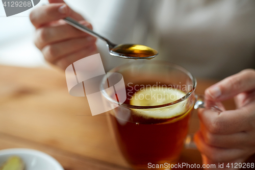 Image of close up of woman adding honey to tea with lemon