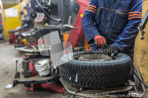 Image of Professional auto mechanic replacing tire on wheel in car repair service.