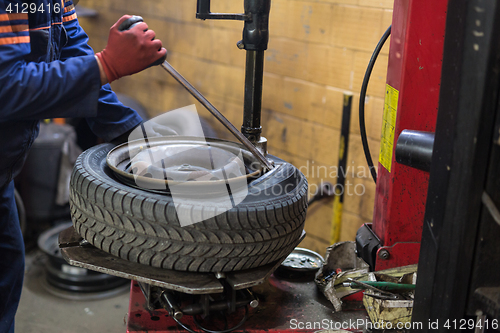 Image of Professional auto mechanic replacing tire on wheel in car repair service.