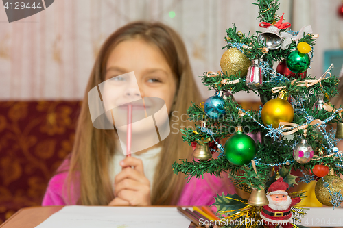 Image of Girl happily thinking about a gift for the new year, focusing on a fur-tree