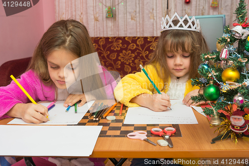 Image of Two girls writing Christmas greeting letter sitting at the table at home