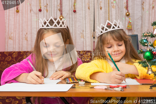 Image of Two girls happily writing a letter to Santa Claus sitting at a desk in the home environment