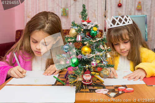 Image of Two girls write a letter to Santa Claus, the focus is on the fur-tree in the middle