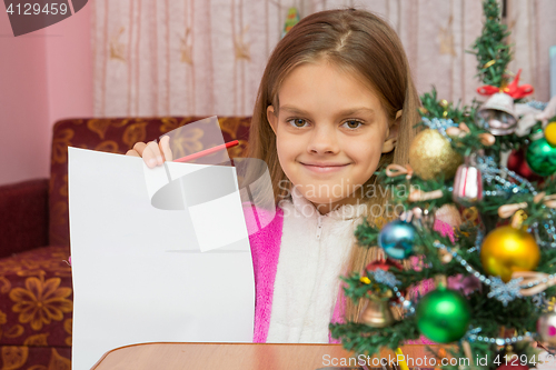 Image of Happy girl shows a sheet of paper at a table in a Christmas setting