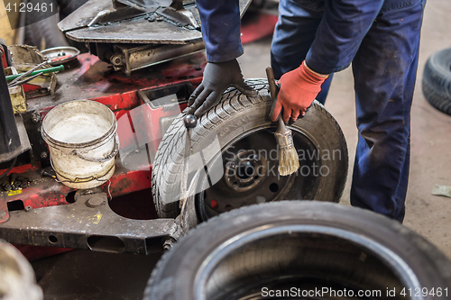 Image of Professional auto mechanic replacing tire on wheel in car repair service.