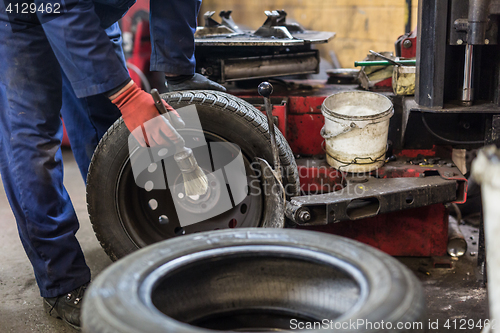 Image of Professional auto mechanic replacing tire on wheel in car repair service.