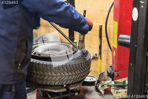 Image of Professional auto mechanic replacing tire on wheel in car repair service.