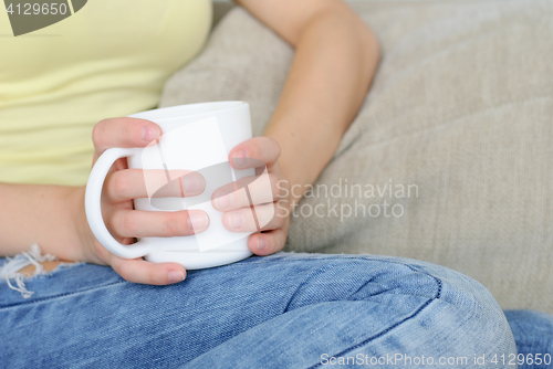Image of young woman sitting on couch and drinking coffee