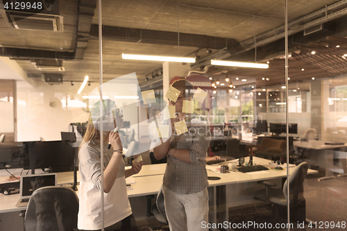 Image of young couple at modern office interior writing notes on stickers