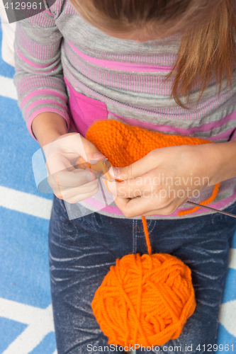 Image of Top view of the child who knits with needles scarf orange thread