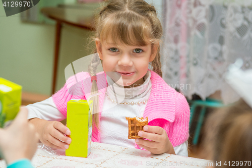 Image of The girl is drinking juice and eating cookies at the desk in the kindergarten