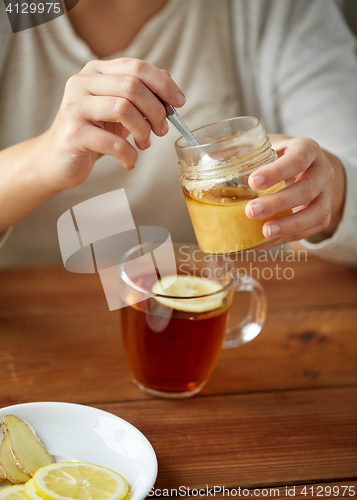 Image of close up of woman adding honey to tea with lemon