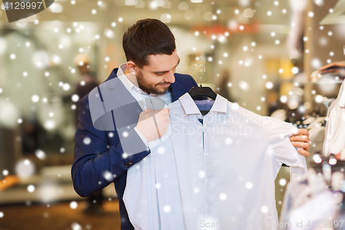 Image of happy young man choosing clothes in clothing store