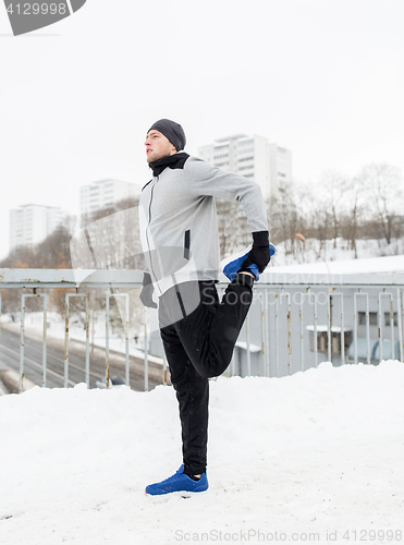 Image of man exercising and stretching leg on winter bridge