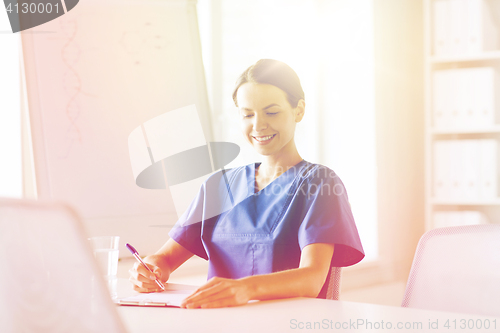 Image of happy female doctor or nurse writing to clipboard