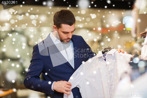 Image of happy young man choosing clothes in clothing store