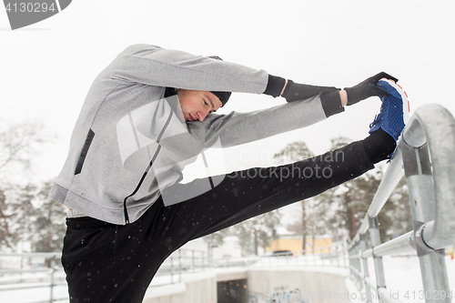 Image of sports man stretching leg at fence in winter