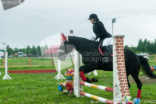 Image of Young girl rider on a horse overcomes obstacles