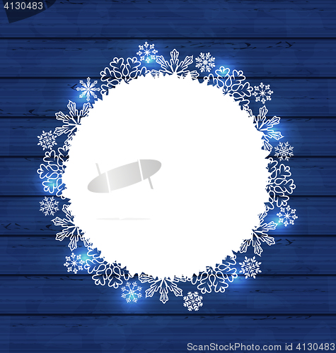 Image of Christmas round frame made in snowflakes on blue wooden backgrou