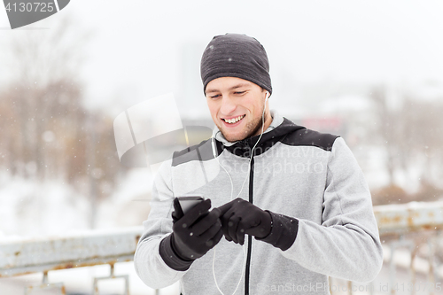 Image of happy man with earphones and smartphone in winter