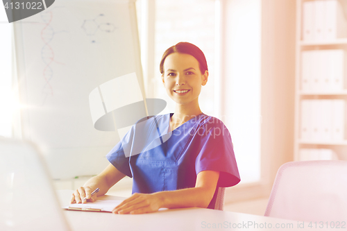 Image of happy female doctor or nurse writing to clipboard