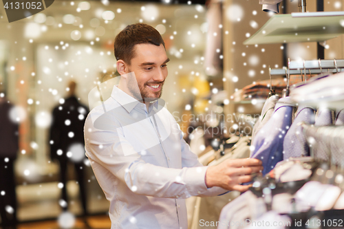 Image of happy young man choosing clothes in clothing store