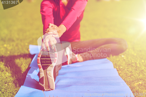 Image of close up of woman stretching leg on mat outdoors