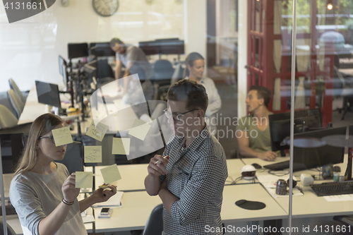 Image of young couple at modern office interior writing notes on stickers