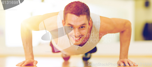 Image of smiling man doing push-ups in the gym