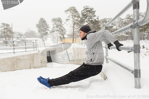 Image of sports man doing triceps dips at fence in winter