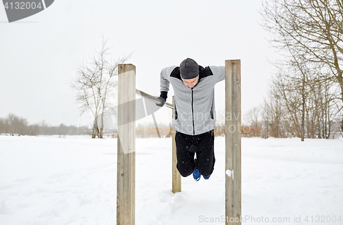 Image of young man exercising on parallel bars in winter